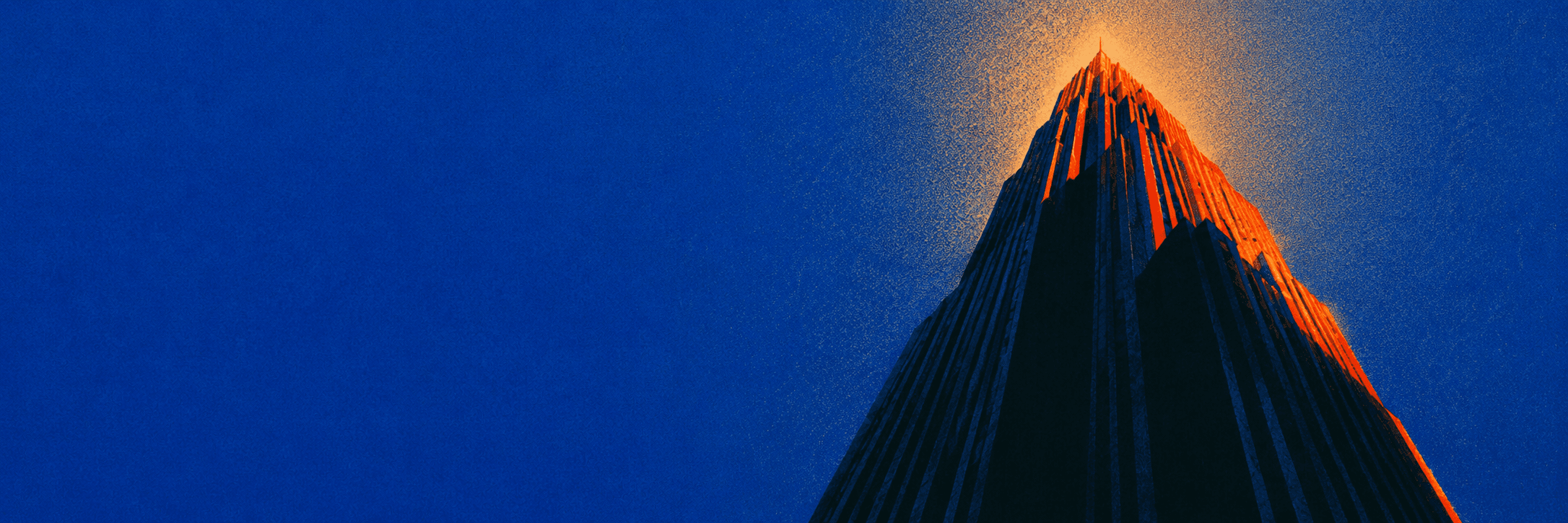 A skyscraper seen from street level, its peak catching orange light against a deep blue sky